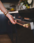 Person opening a kitchen oven with a brass and copper appliance handle, artisan hardware design.