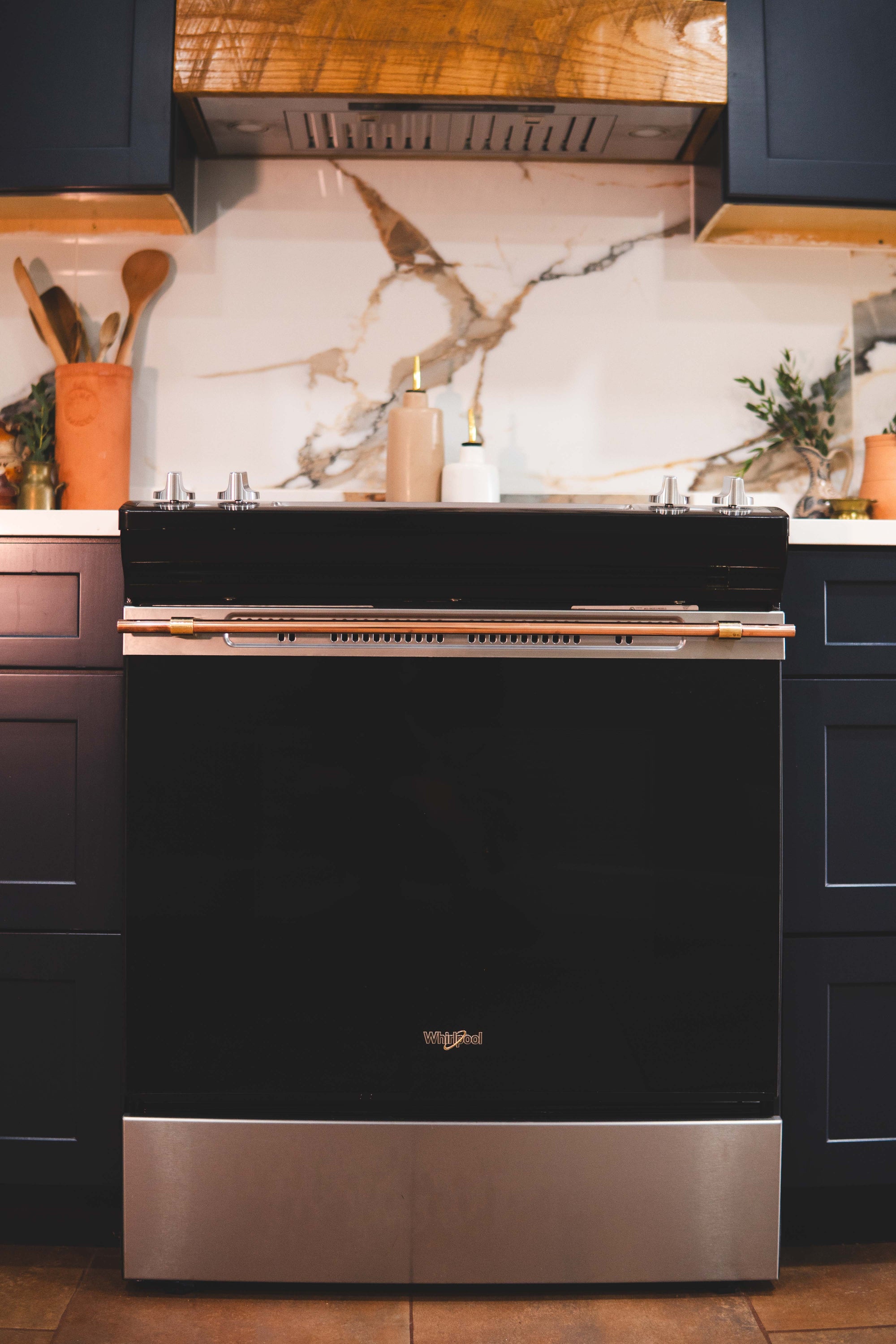 Brass and copper appliance handle installed on a Whirlpool range oven in a modern kitchen.