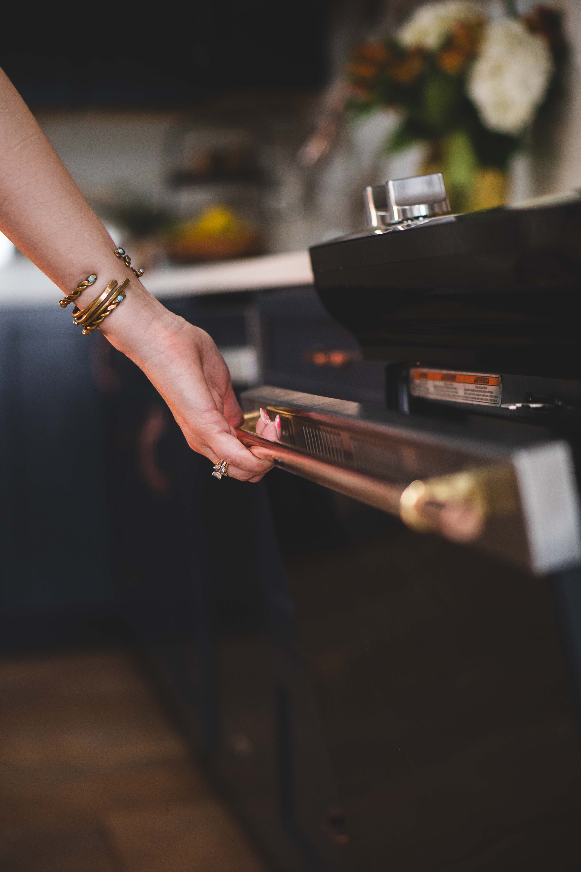Person opening a kitchen oven with a brass and copper appliance handle, artisan hardware design.