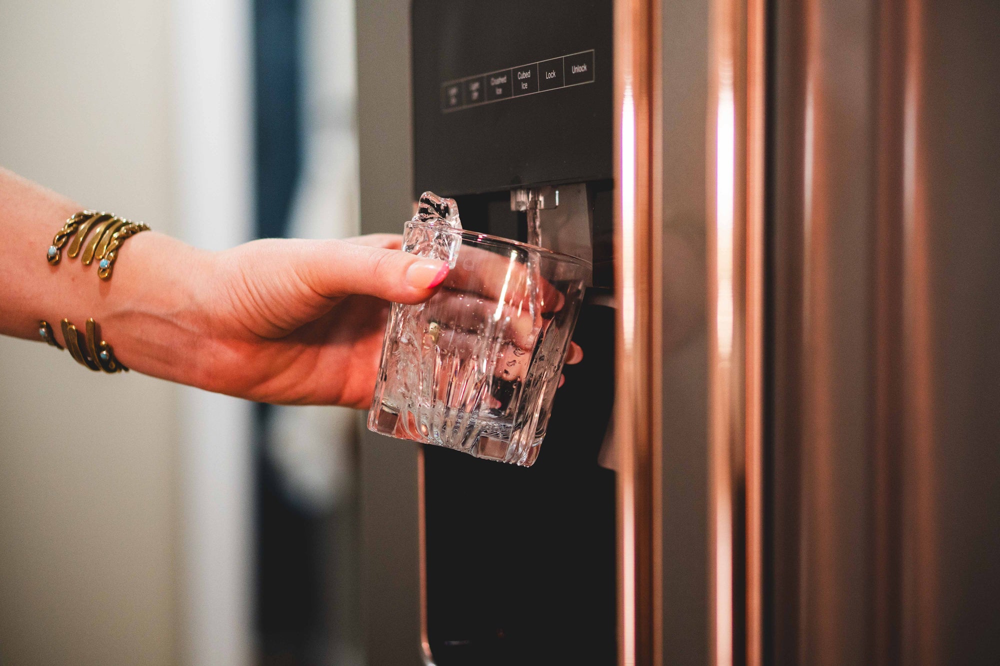 Person getting a drink from a Whirlpool stainless steel side by side refrigerator that displays an interchangeable appliance handle for stainless steel appliances